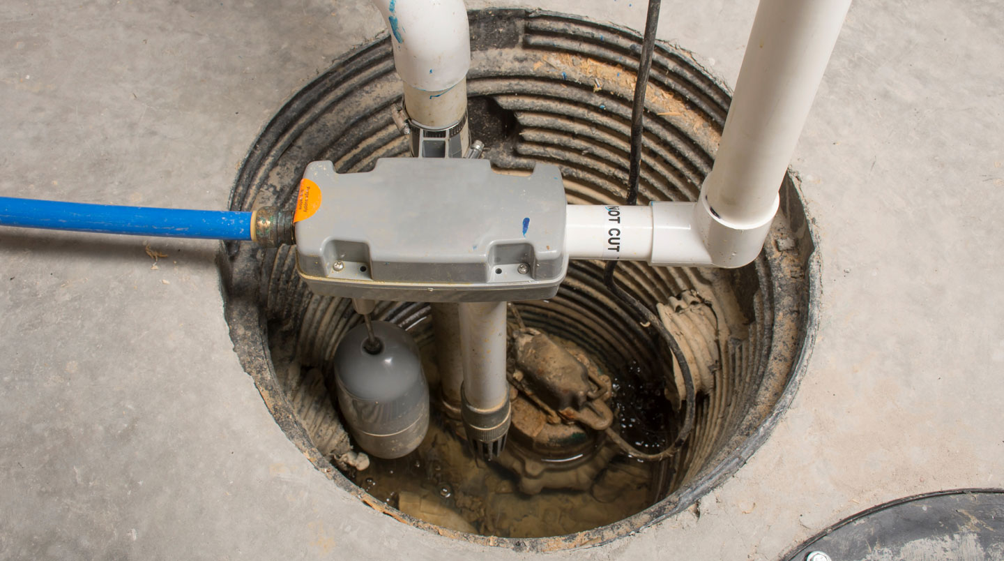 Pompe de puisard installée dans un puisard de sous-sol résidentiel avec tuyaux d'évacuation PVC et flotteur visible, eau présente montrant le système en fonction